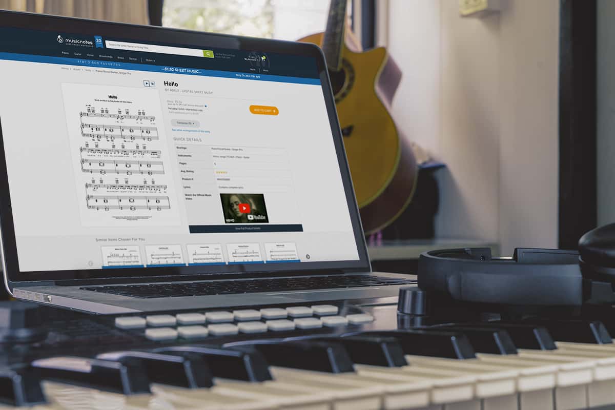 一台显示数字乐谱的笔记本电脑放在合成器上，背景是吉他